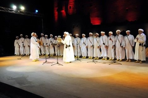 Femmes en robes brodées et foulards rouges, rangée de danseuses d'Ahwach devant un grand tambour (ganga), scène de nuit, Ouarzazate 2012.