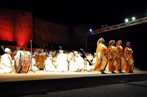 Vue d'ensemble d'une troupe d'Ahwach (hommes aux tambours au centre, femmes autour) sur une scène éclairée, Kasbah en arrière-plan, Ouarzazate 2012.