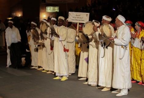 Carnaval d'ouverture : troupes en djellabas claires avec bendirs défilant derrière une pancarte, Ouarzazate, novembre 2013.