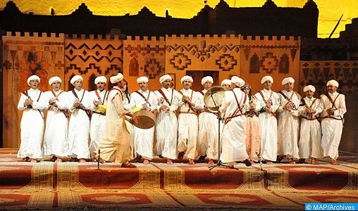 Troupe d'Ahwach en blanc alignée sur une scène décorée de motifs berbères, tapis rouges; photo d'archives de la MAP illustrant l'annonce de la 5e édition (11–13 août 2016).