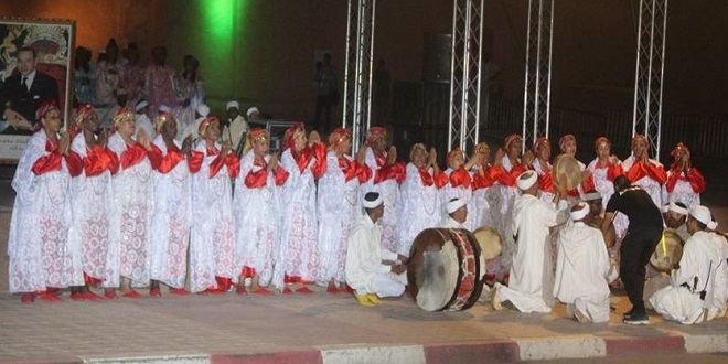 Troupe féminine d'Ahwach en robes blanches à motifs rouges et musiciens avec bendirs et ganga, sous un portrait royal, ouverture 2017.