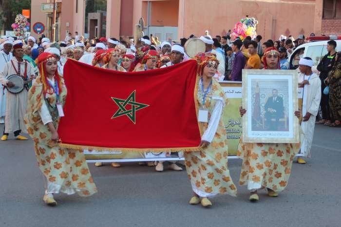 Carnaval d'ouverture : troupe en robes dorées portant le drapeau et le portrait royal devant une foule, 12 mai 2023.