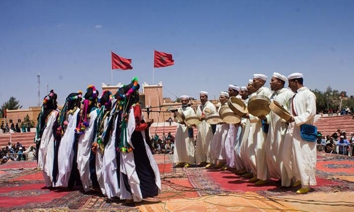 Danseuses en robes blanches à motifs et foulards multicolores, musiciens aux bendirs, drapeaux marocains, en plein air à Ouarzazate; illustration de l'annonce de la 11e édition (L'Opinion, 9 mai 2023), reprise par Finances News (13 mai 2023) et Quid (octobre 2026).